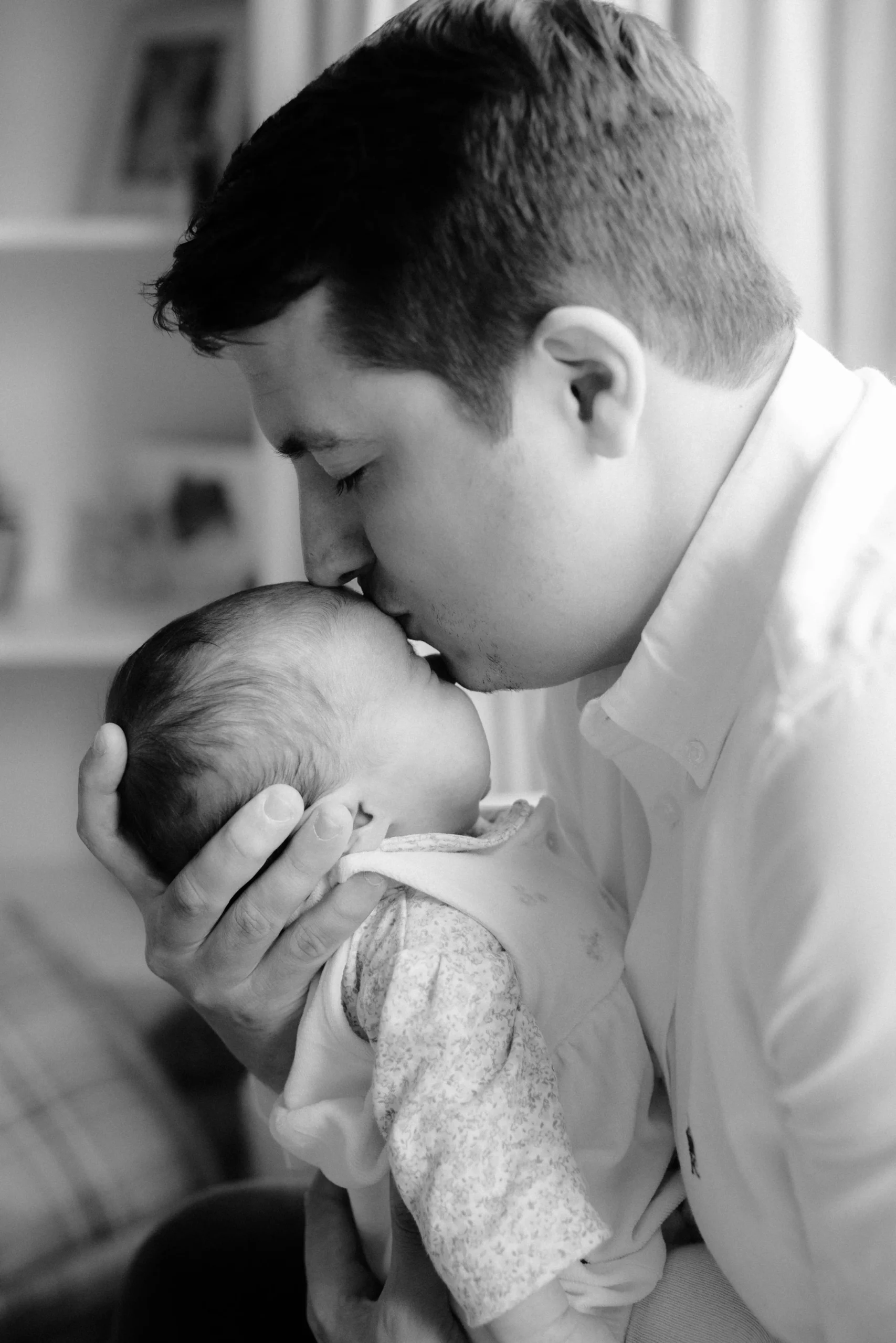 A man holding a baby, gently kissing the baby's forehead in a black and white photo.