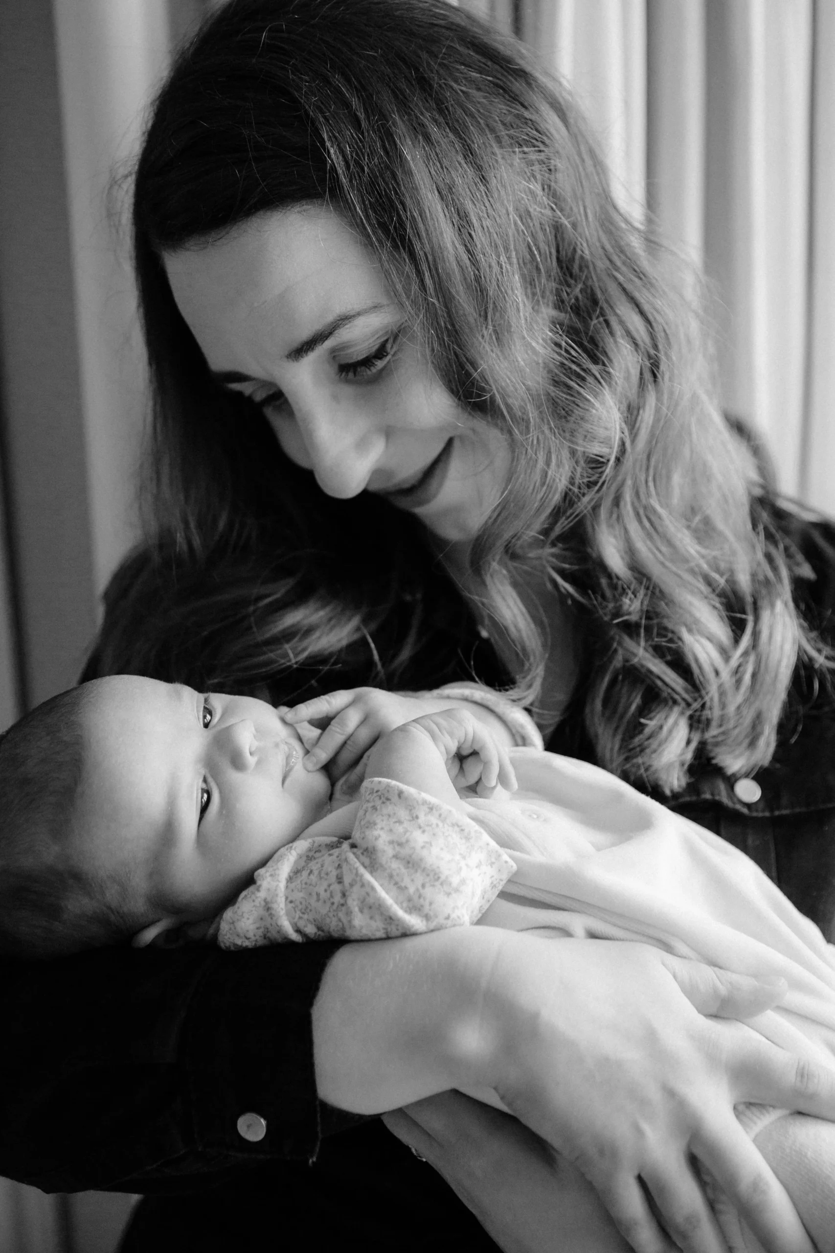 A woman holding a baby in her arms, smiling and looking down at the baby, who is lying on her arms and gazing up at her, in black and white.