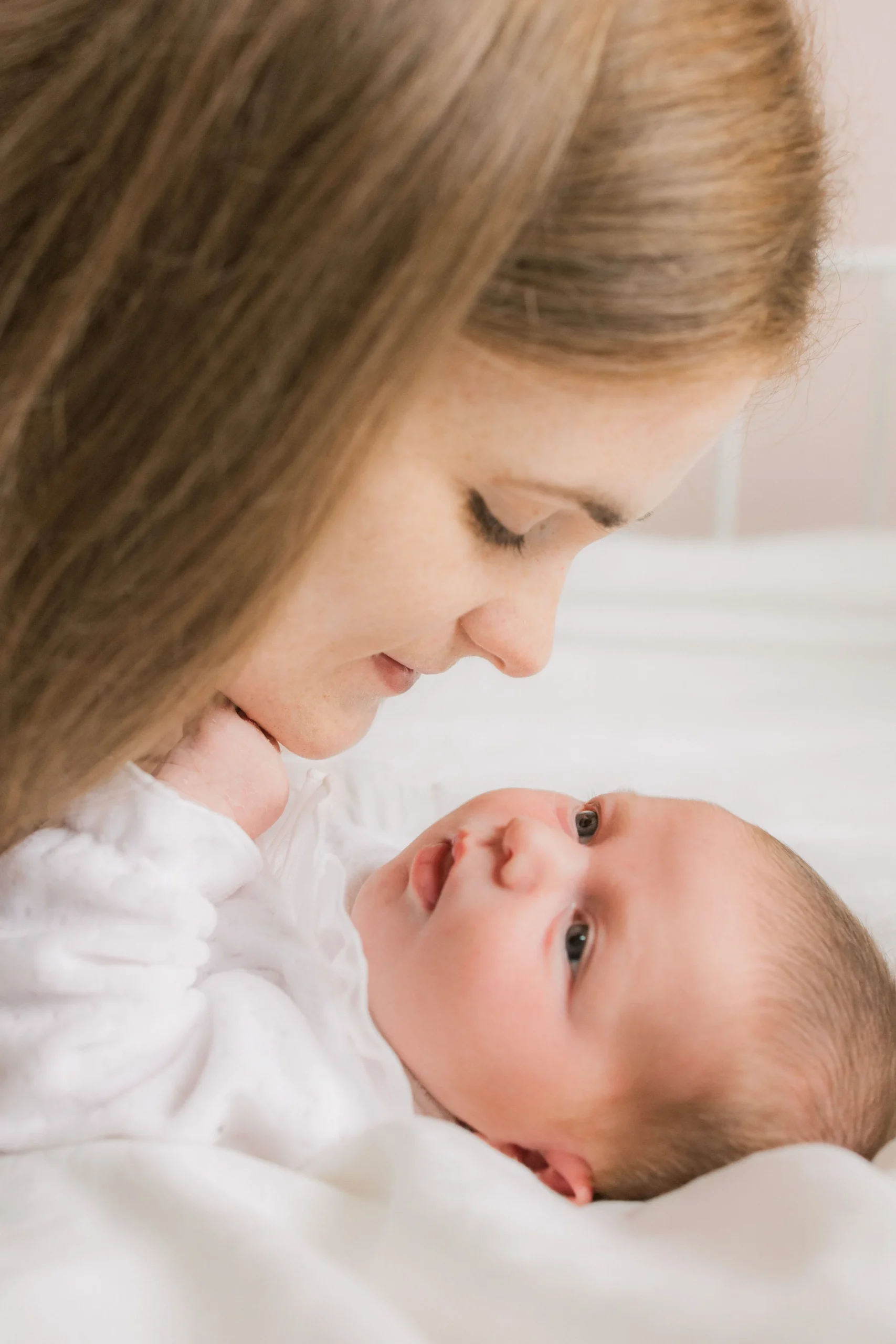 Close-up of a mother smiling down at her newborn baby lying on a white surface.