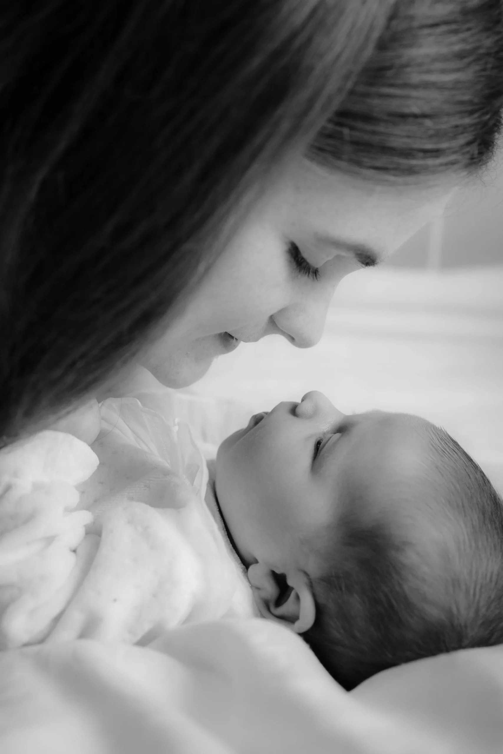A woman and a baby sharing an intimate moment, with their noses almost touching, in black and white.