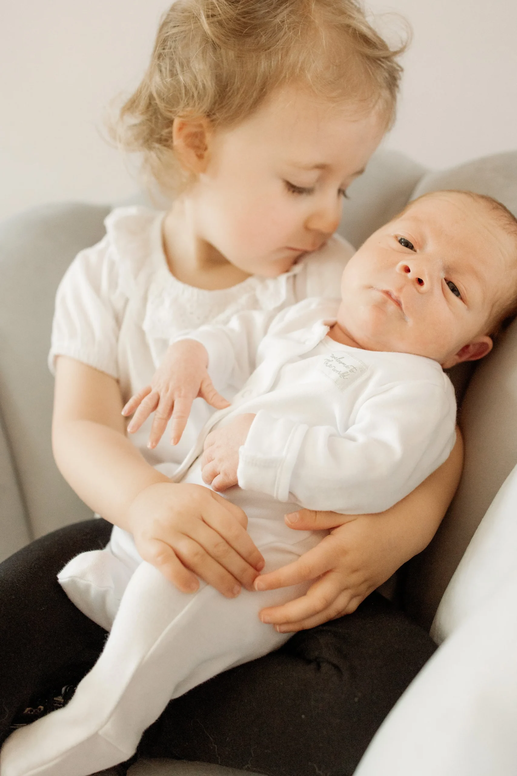 A young girl holding a baby. The girl is looking at the baby, who is looking at the camera.